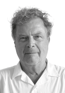 Svartvitt porträttfoto av Pelle Hasselgren. Han är en medelålderns man med lockigt hår, klädd i en vit skjorta med krage.